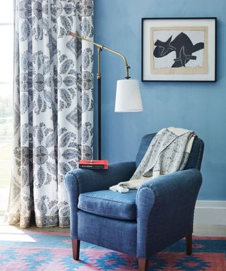 blue armchair against blue wall and blue patterned curtains