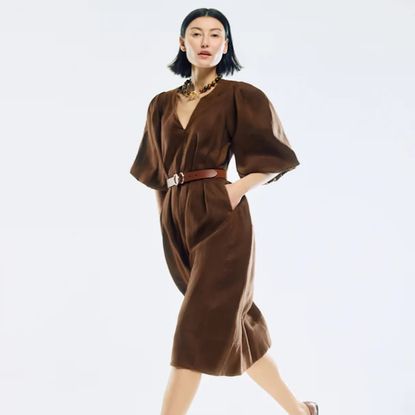 A woman posing in a brown Jigsaw dress with her hands in her pockets on an off-white background