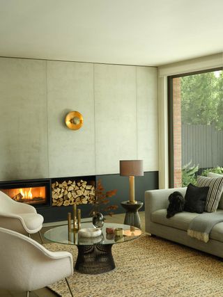 A neutral living room with a modern fireplace and a gold sculptural wall light above a log pile