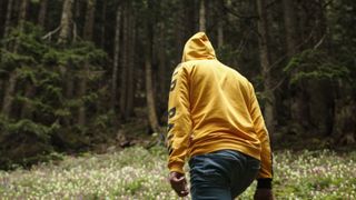 A man hiking in the forest wearing a yellow hoodie