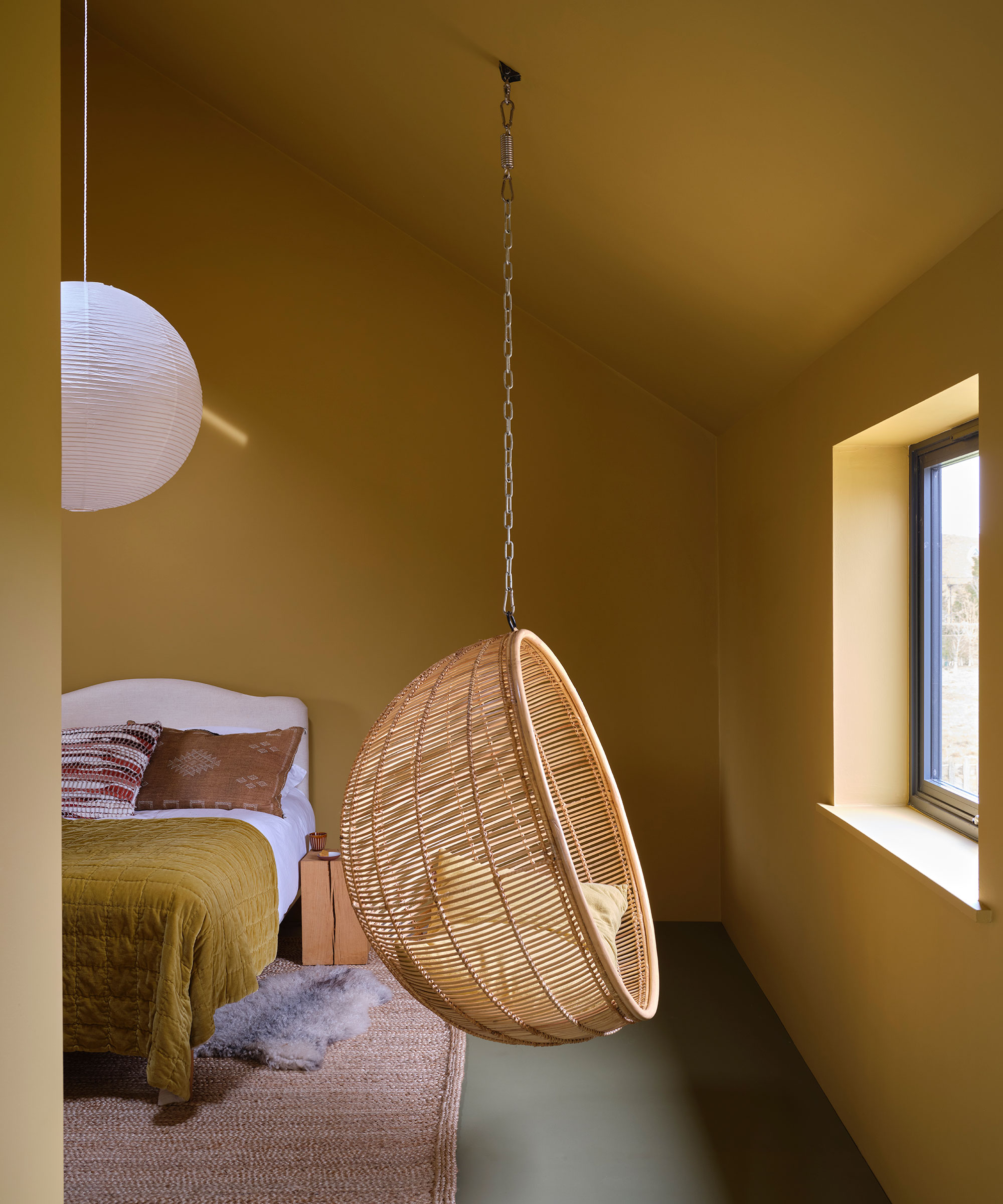 yellow bedroom painted in Farrow &amp;amp; Ball paint with a wicker hanging chair