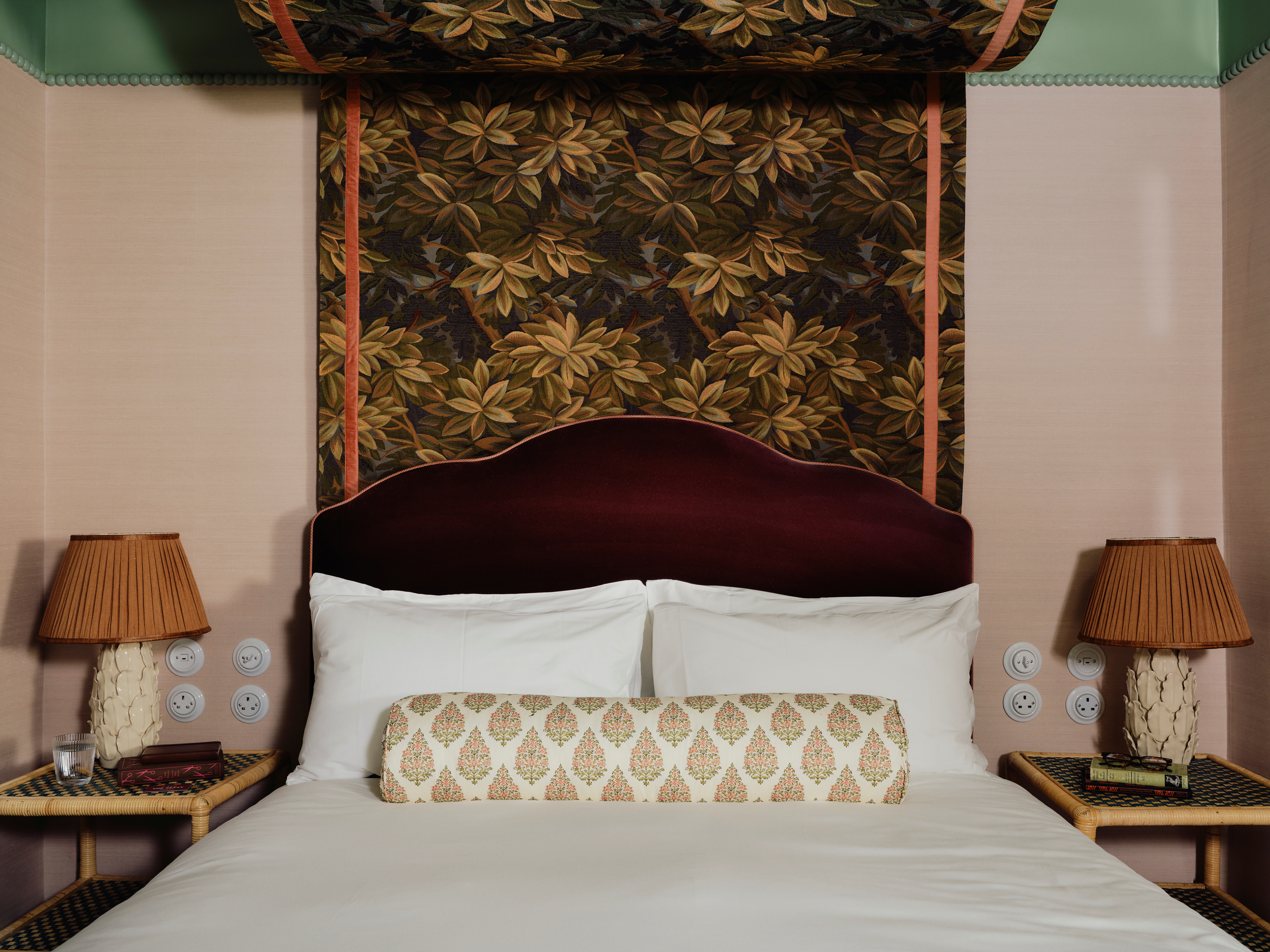 A maximalist hotel room filled with earthy tapestries, dust pink and mint green walls, textural bedside table lamps, eccentric prints and fabrics, and more.