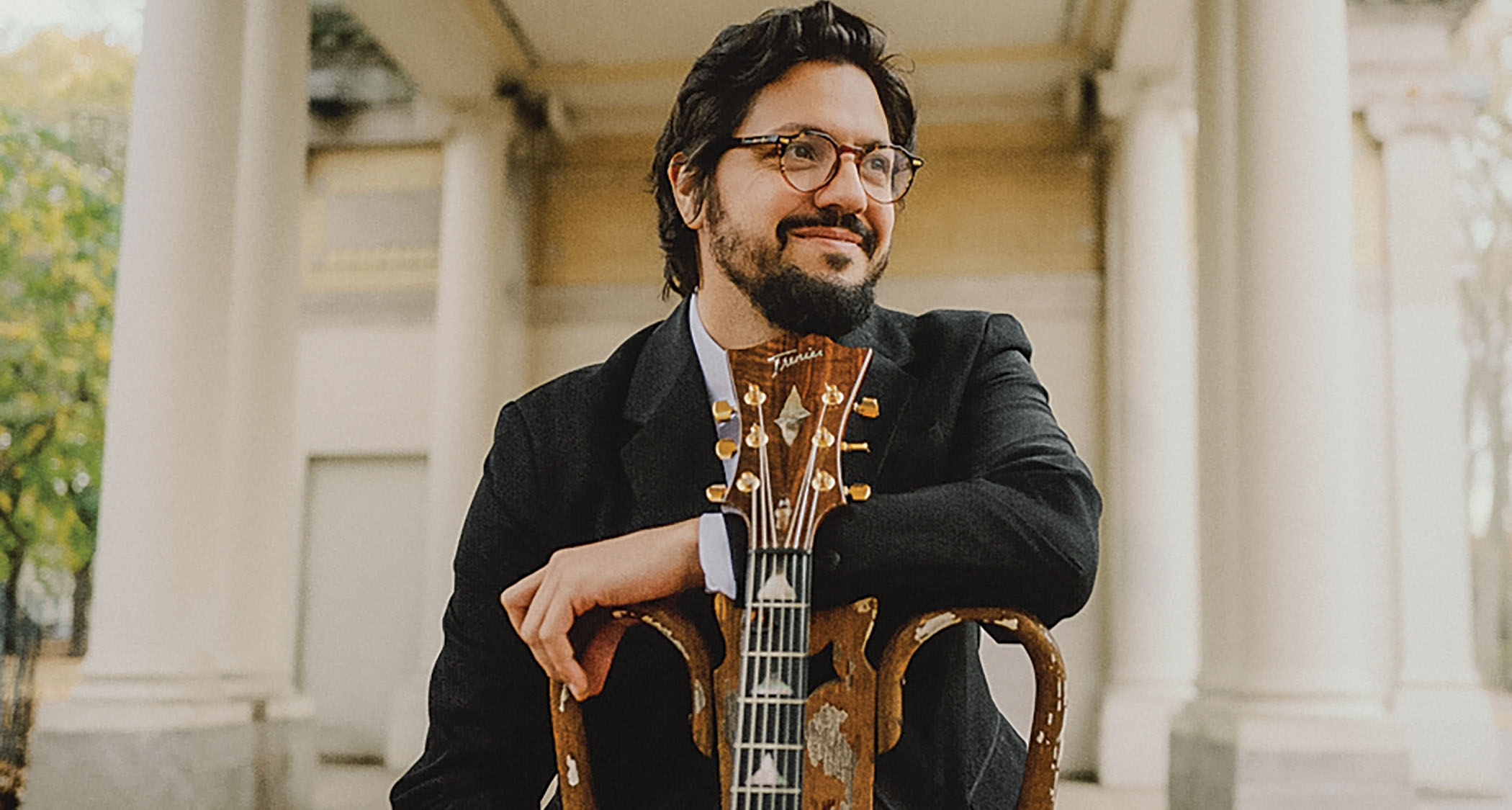 A dapper looking Pasquale Grasso smiles as he sits on a chair with his Trenier signature model