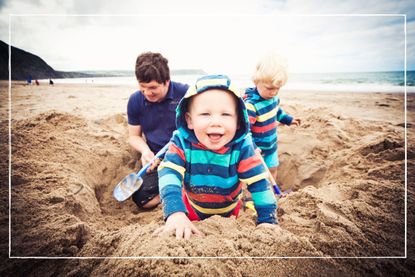 Father and two children in matching jumpers digging a hole at the beach