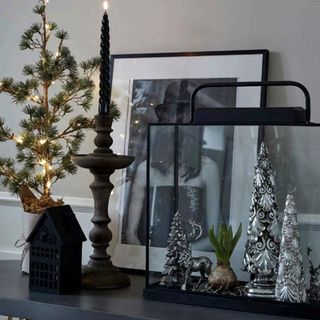 Black Christmas mantel piece next to a small tree branch with fairy lights and a picture frame