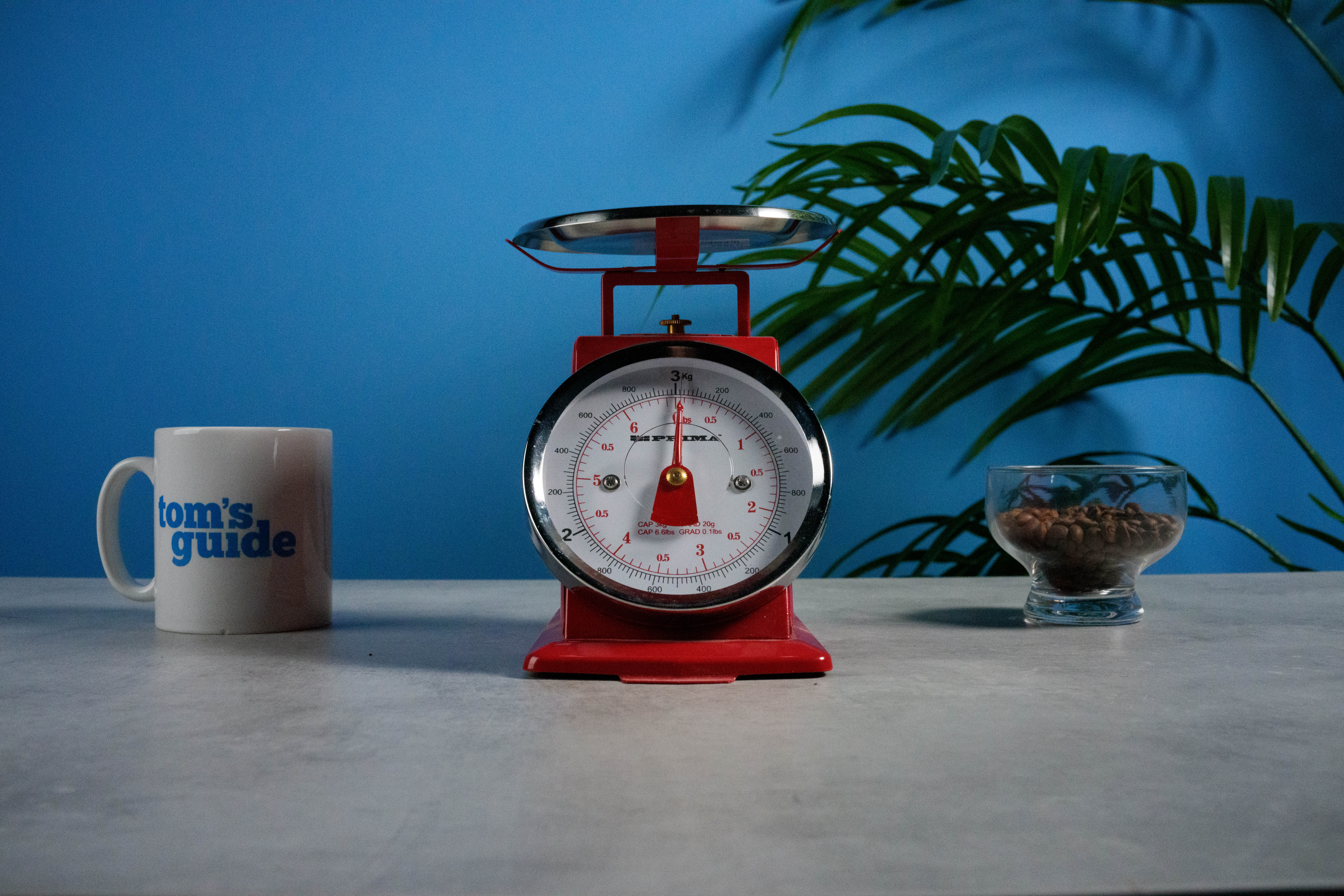 A photo of a set of red scales next to a Tom's Guide mug and some coffee beans, with a blue wall in the background