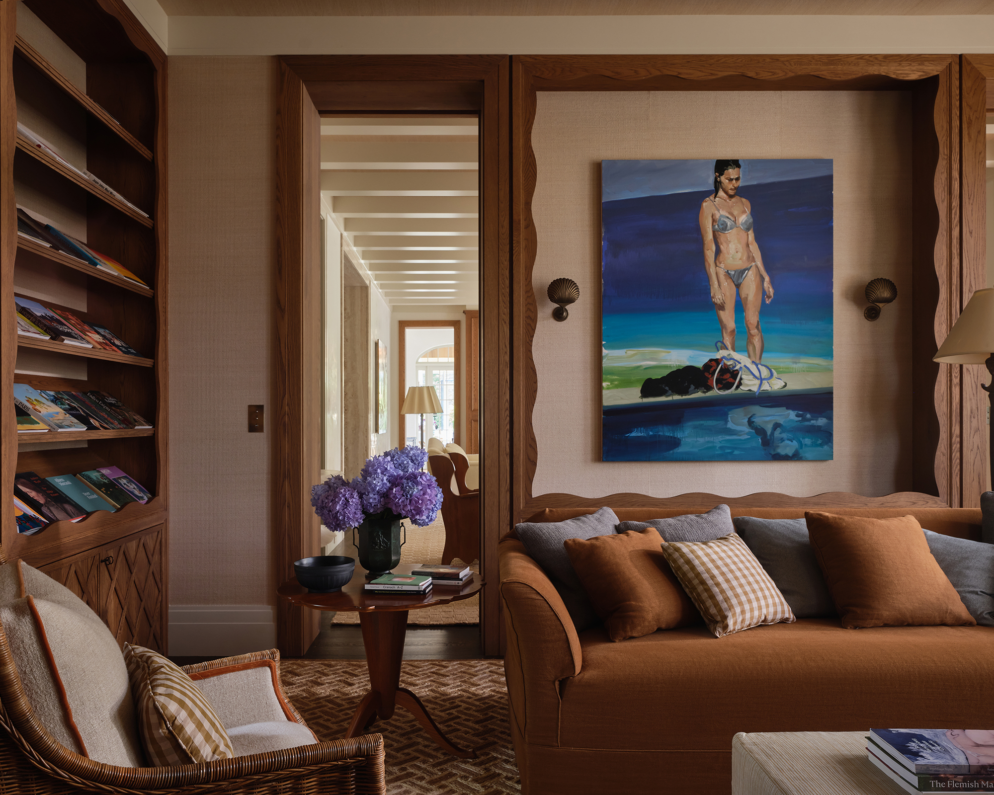 living room with large artwork on the wall above a rust colored sofa. Along one wall is a wood bookcase