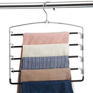 A multi-pants hanger with five different colored trousers hanging from it. on a silver clothes rail.