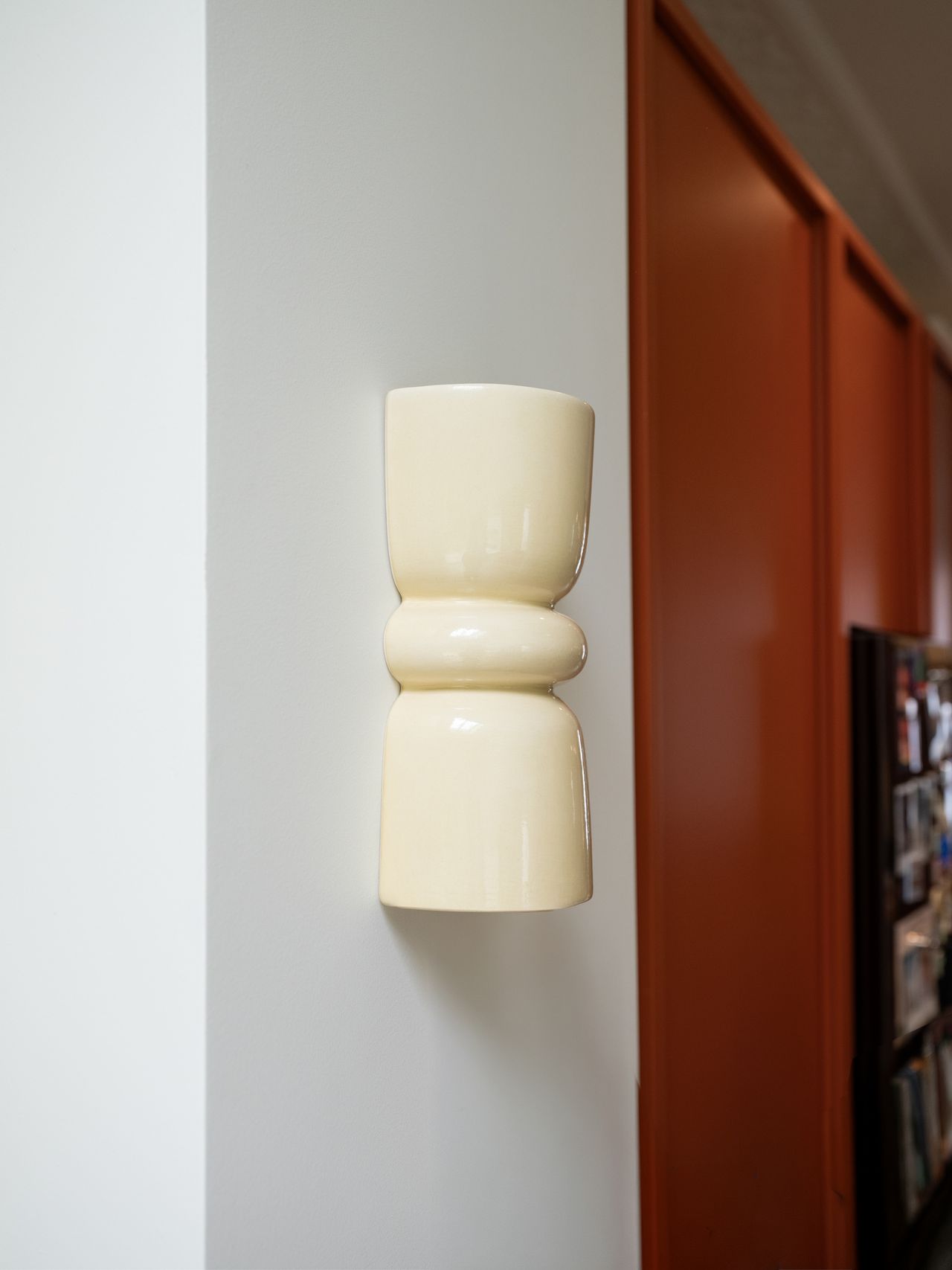 Image of a sculptural, butter yellow sconce light on a white wall.