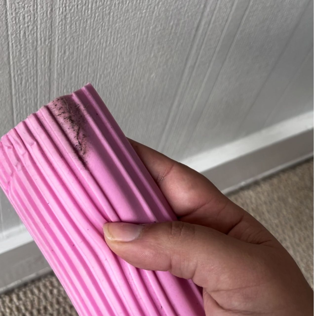 Hand holding pink Damp Duster with visible dust on it with skirting boards and white wallpaper in the background
