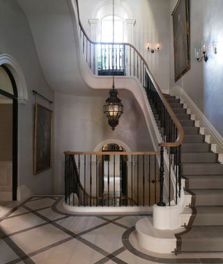 Open and light stairway with white and grey staircase and marble flooring. Glass chandler