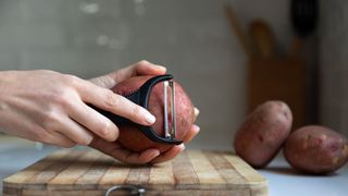 A person peeling potatoes with a vegetable peeler