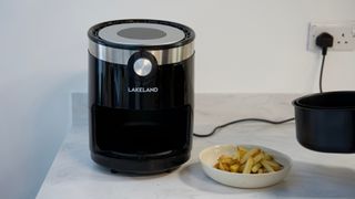 An air fryer on a white marble kitchen countertop with a bowl of chips