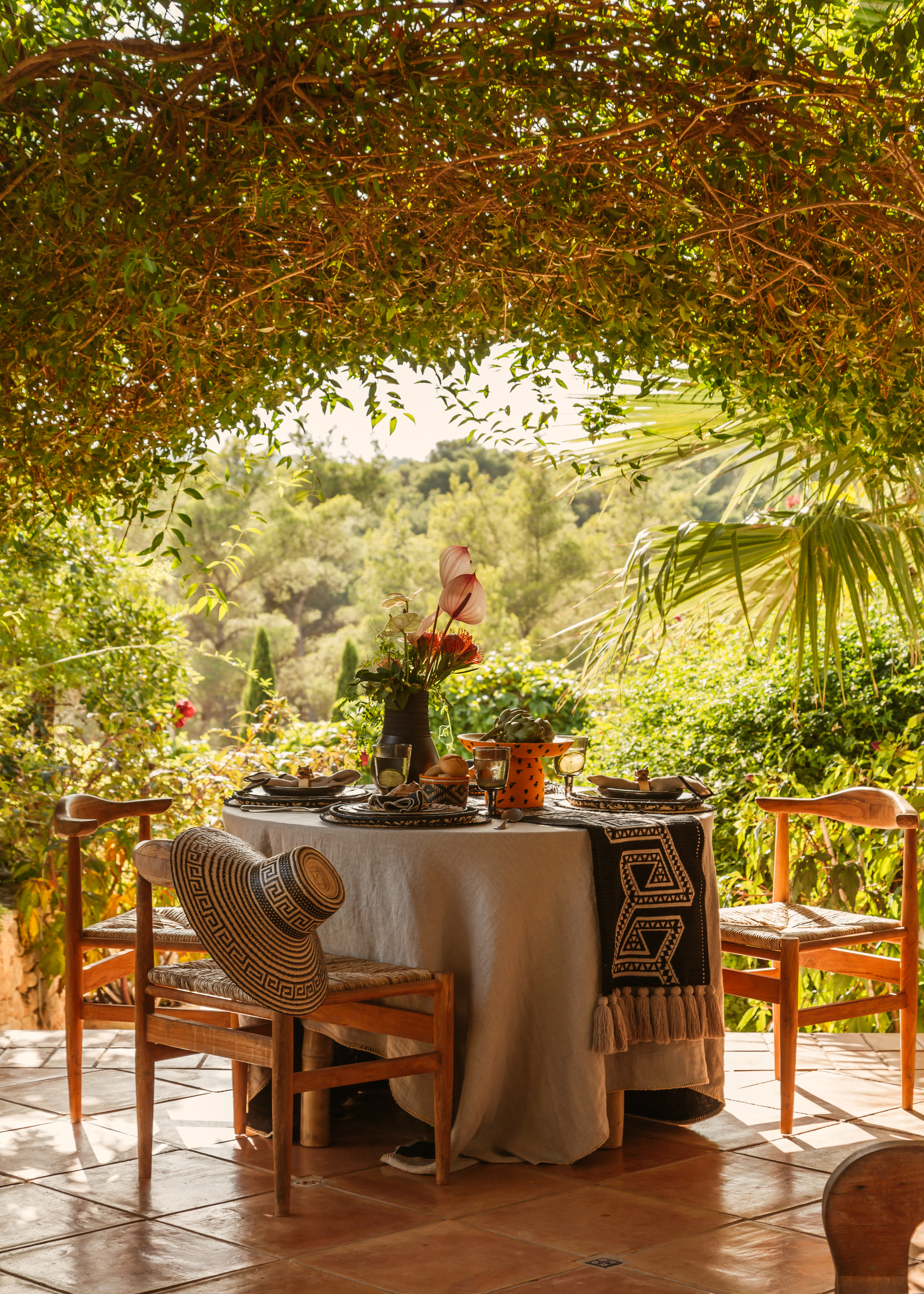 A circular outdoor dining table on a veranda under an arch of foliage