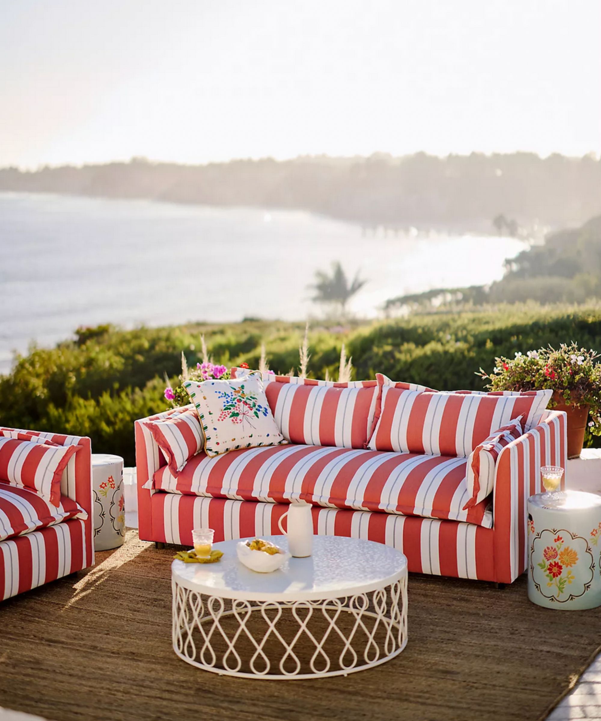 Red and white striped outdoor sofa and armchair with white metal coffee table and a sea view in the background