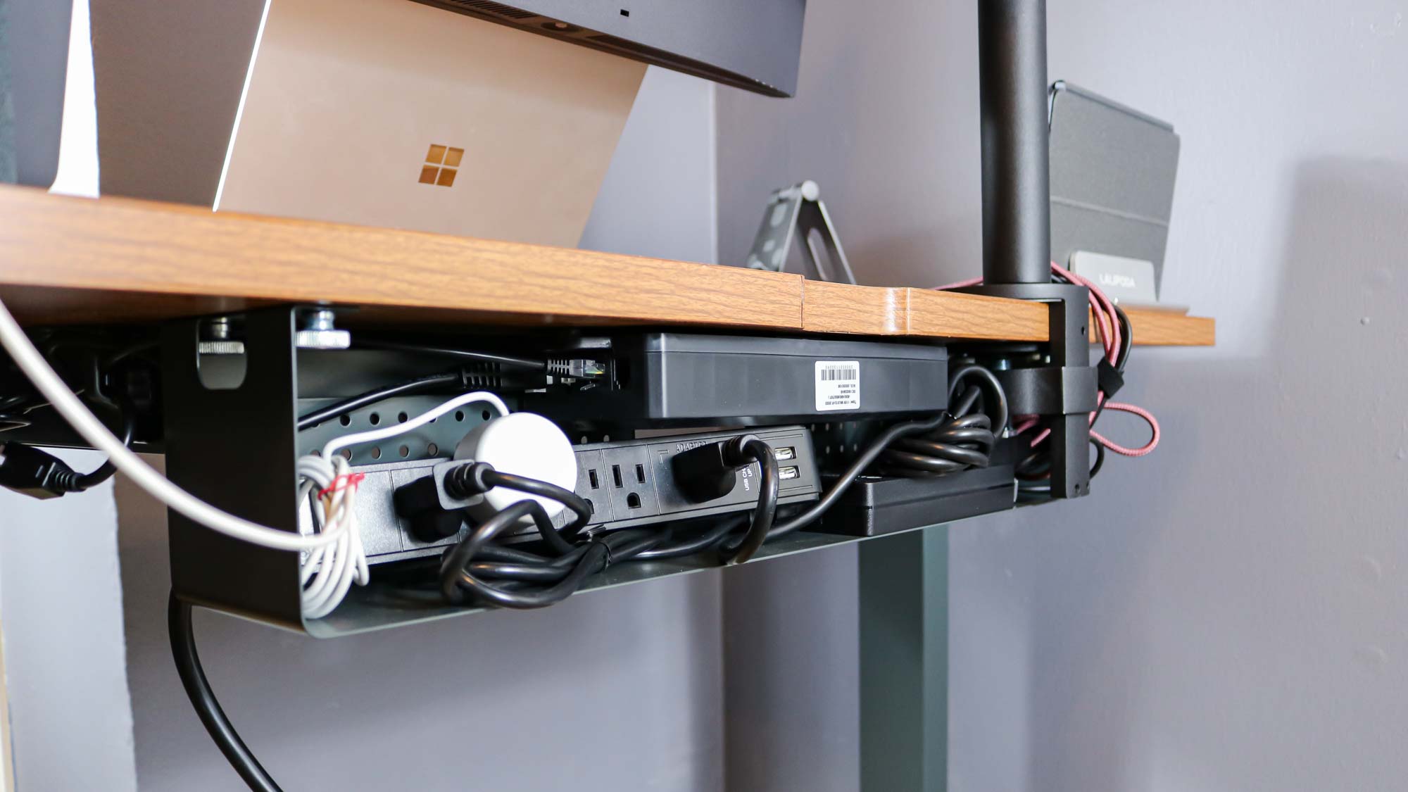 The Branch Duo Standing Desk's cable management tray filled with a surge protector and various cables
