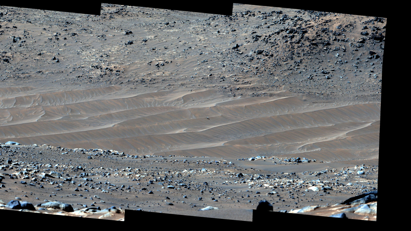 long-distance view of rippling sand dunes, with a tiny drone resting in the middle of them