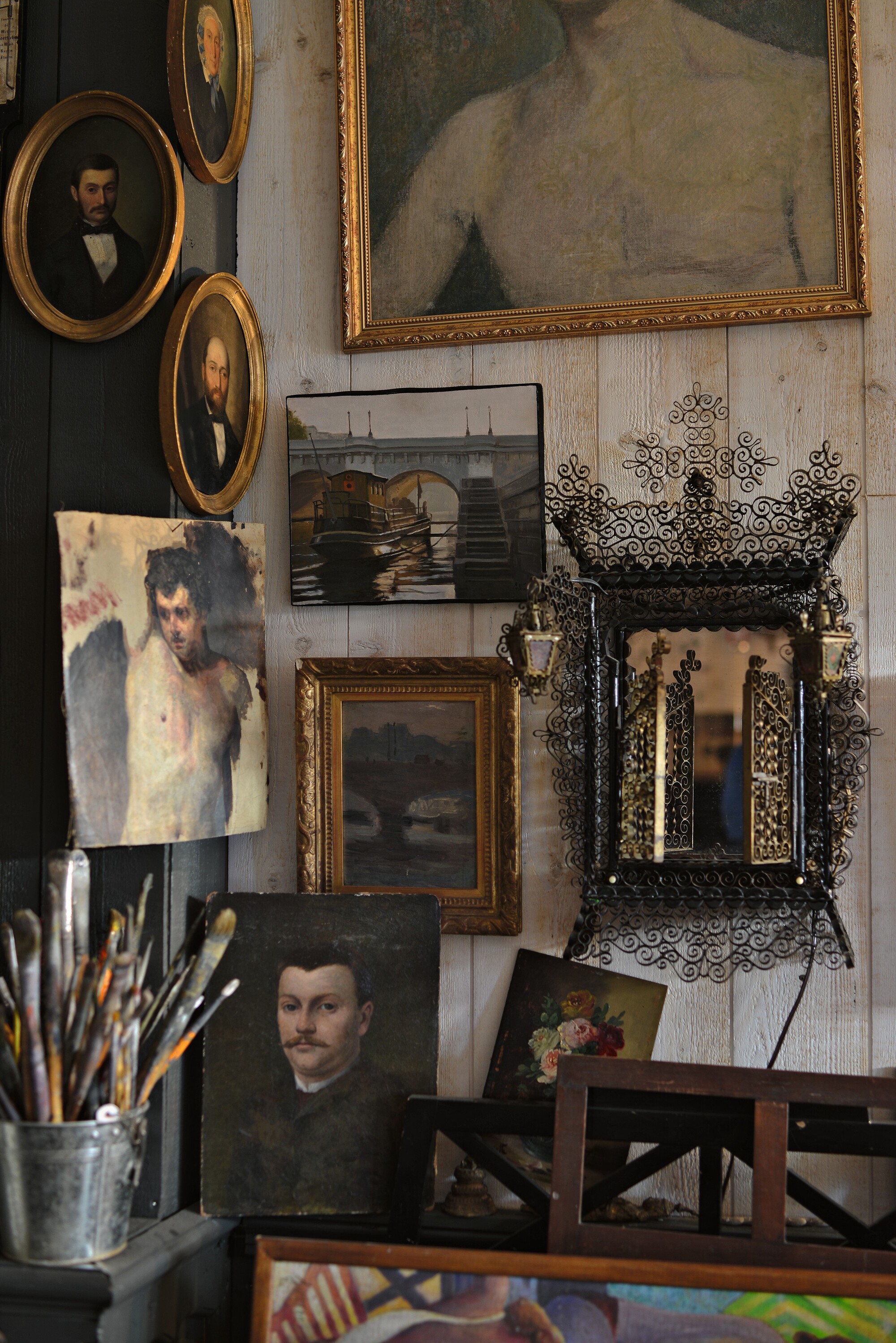 a corner of antique oil paintings and artworks hung on the wall, with paint brushes, and frames
