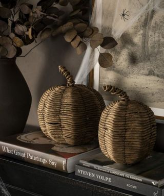 pair of wicker pumpkins styed on table with books and vase of dried eucalyptus