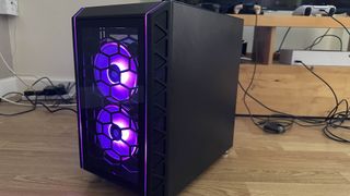 A Refract Gaming Jade PC with purple lighting on, sitting on a wooden floor