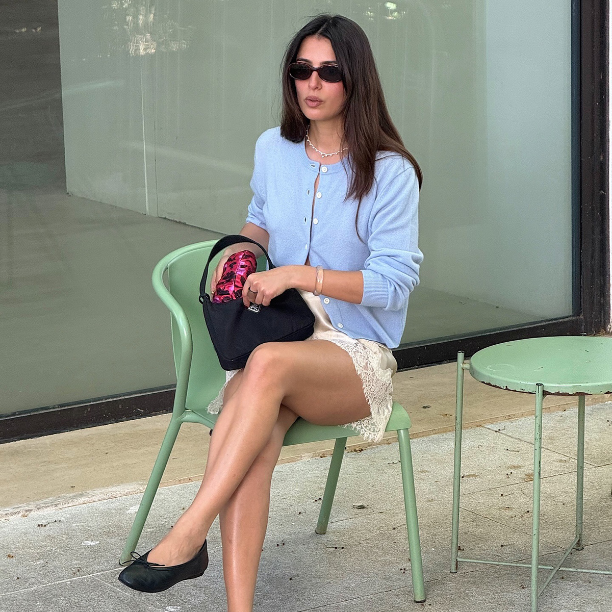 French influencer Tamara Mory wearing a light blue cardigan, cream lace-trimmed miniskirt, and bkack ballet flats
