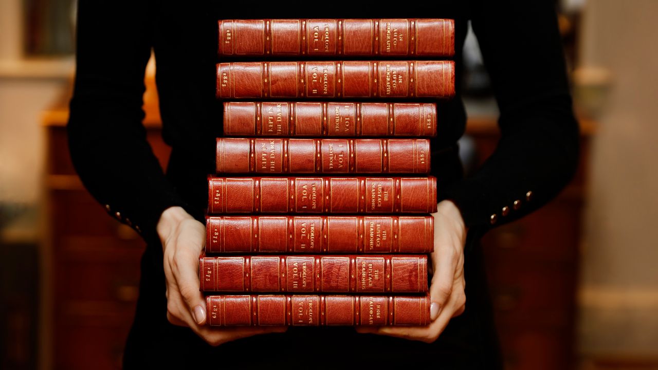 A person carrying a stack of leather-bound books