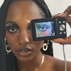 An image of a woman with heavy eye makeup and a digital camera in front of one eye.