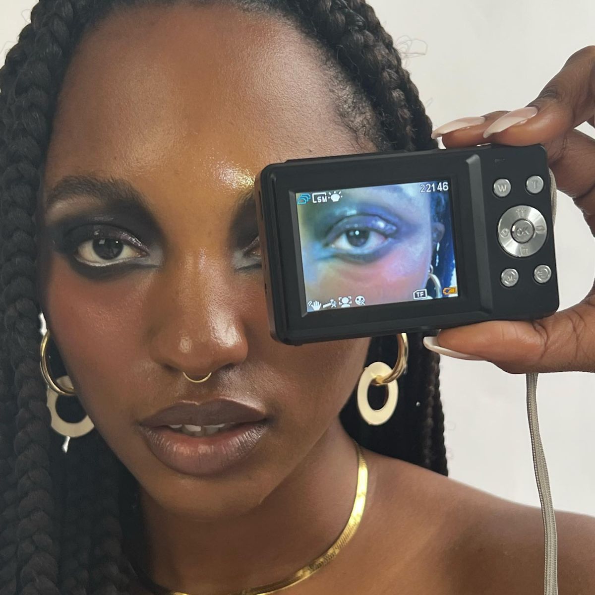 An image of a woman with heavy eye makeup and a digital camera in front of one eye.