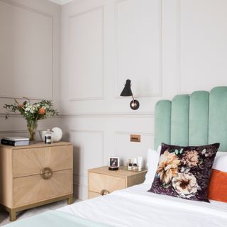 White painted bedroom with panel moulding feature wall, bed with teal headboard, bedside table and chest of drawers