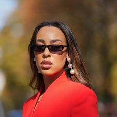 Woman wearing sunglasses with brunette hair, pearl earrings and red jacket - SPF with benefits