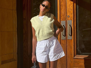 woman wearing yellow vest sweater, white linen shorts, and loafers