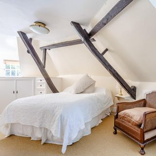 bedroom with white wall bed wooden beams on wall and brown chair