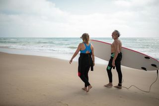 Couple on a beach carrying surfboards