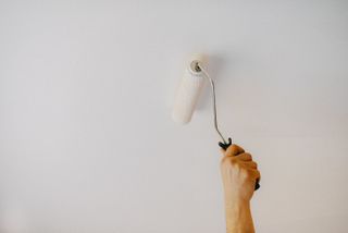 Someone using a roller of white paint to paint a ceiling
