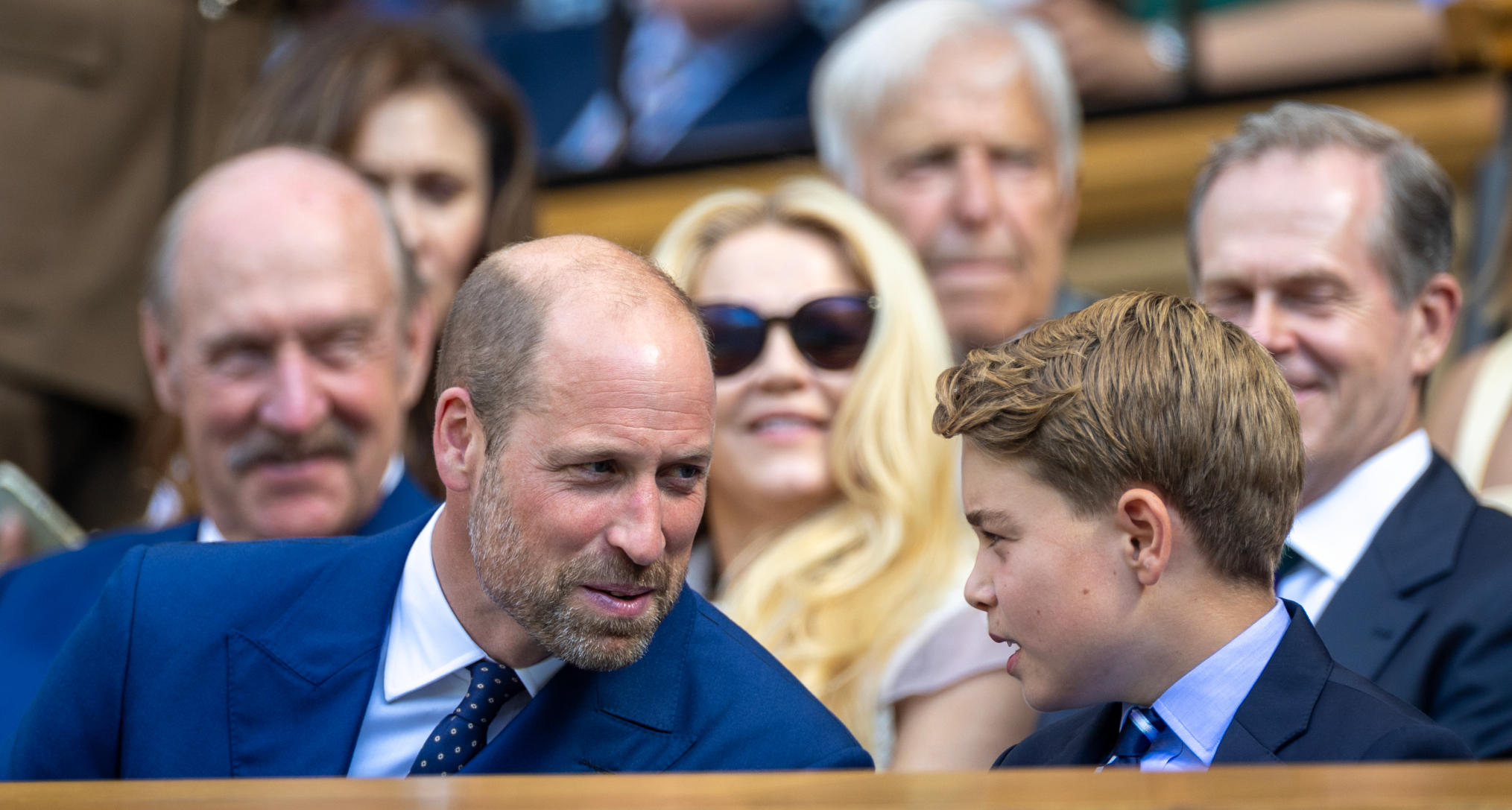 Prince William smiling sitting next to Prince George at Wimbledon and leaning towards him