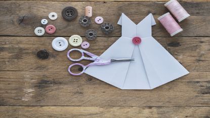 Paper sewing: Small paper dress on table amongst sewing equipment 