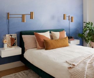 blue bedroom with green upholstered bed and brass wall lamps