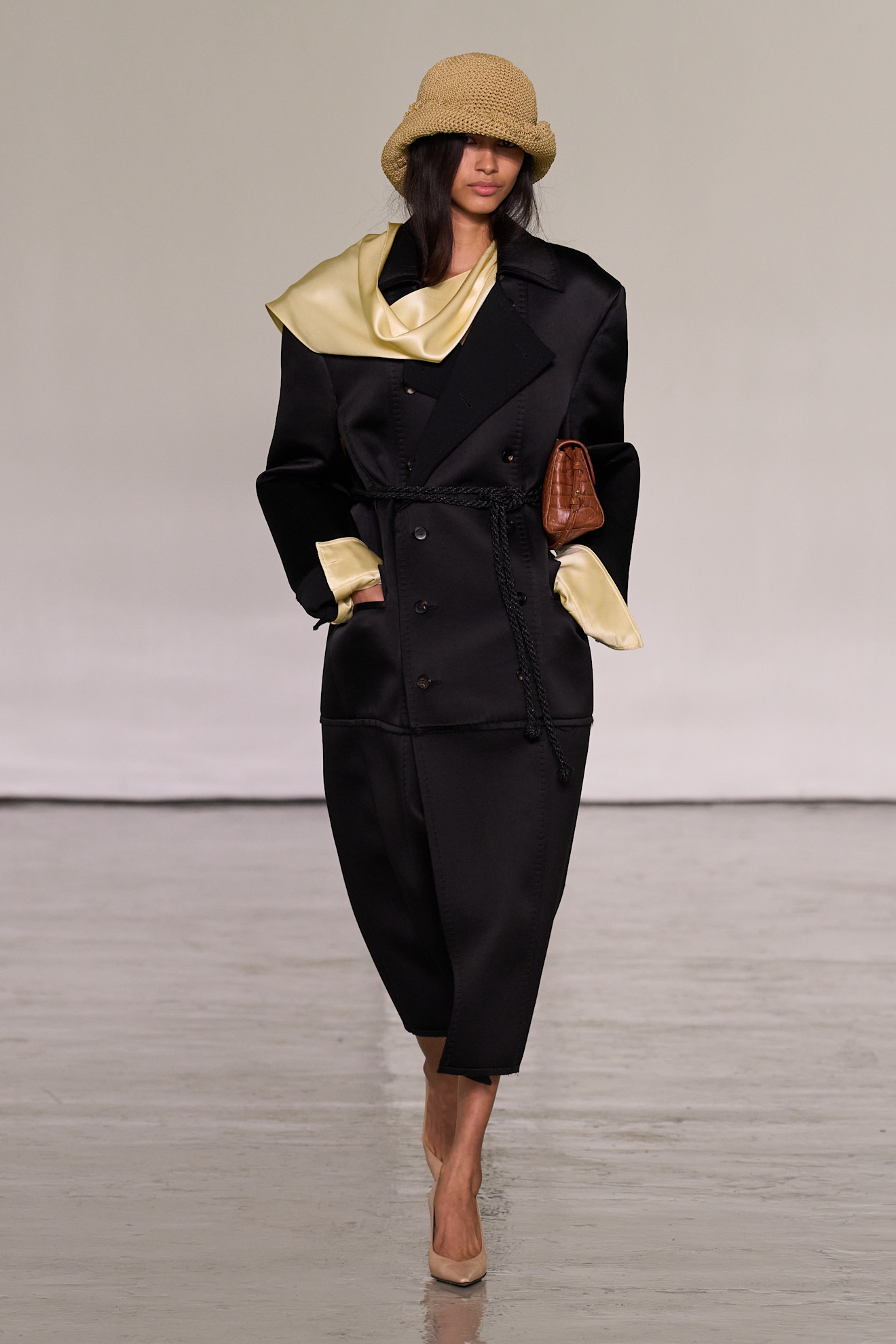 A model walking in the spring/summer 2027 Bottega Veneta show during Milan Fashion Week wearing a knit hat with a black coat.