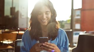 Woman in a sunny room looking at a smartphone while smiling