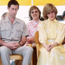 Prince Charles looking down and wearing a tan shirt sitting next to Princess Diana wearing a yellow dress and frowning