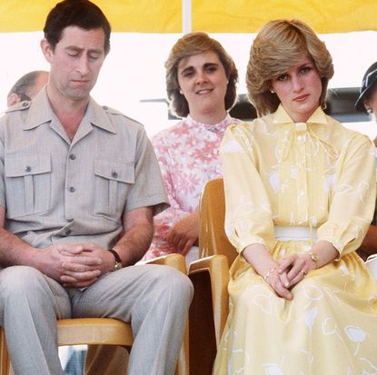 Prince Charles looking down and wearing a tan shirt sitting next to Princess Diana wearing a yellow dress and frowning