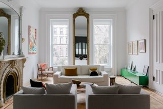 A large white living room with tall full length windows and a statement stone fireplace with an overmantel mirror