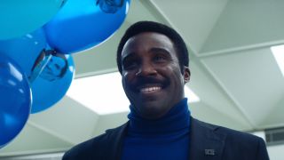 Tramell Tillman as Mr. Milchik, smiling with blue Mark balloons in his hand in Severance Season 2
