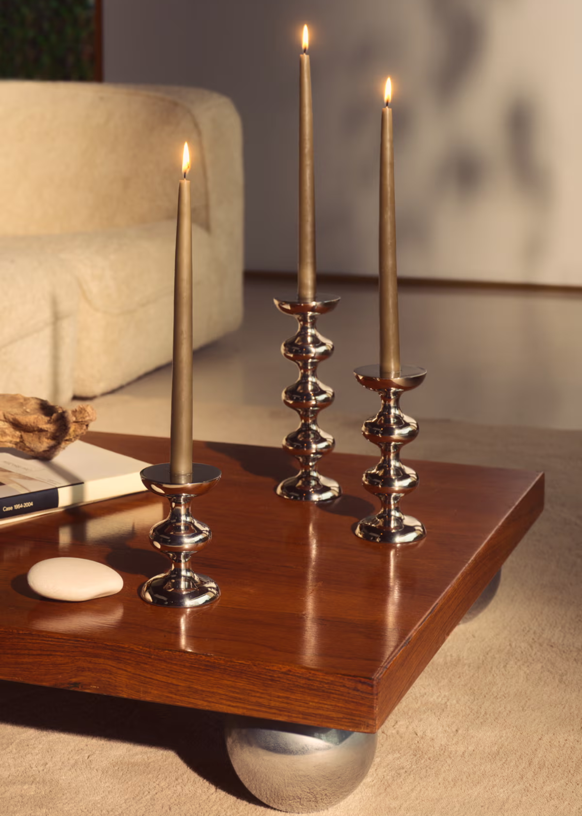 A low wood table with bobbin-style metal feet and a trio of brown tapered candles on chrome candle holders
