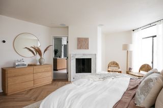 A modern bedroom with light wooden furniture and a marble fireplace
