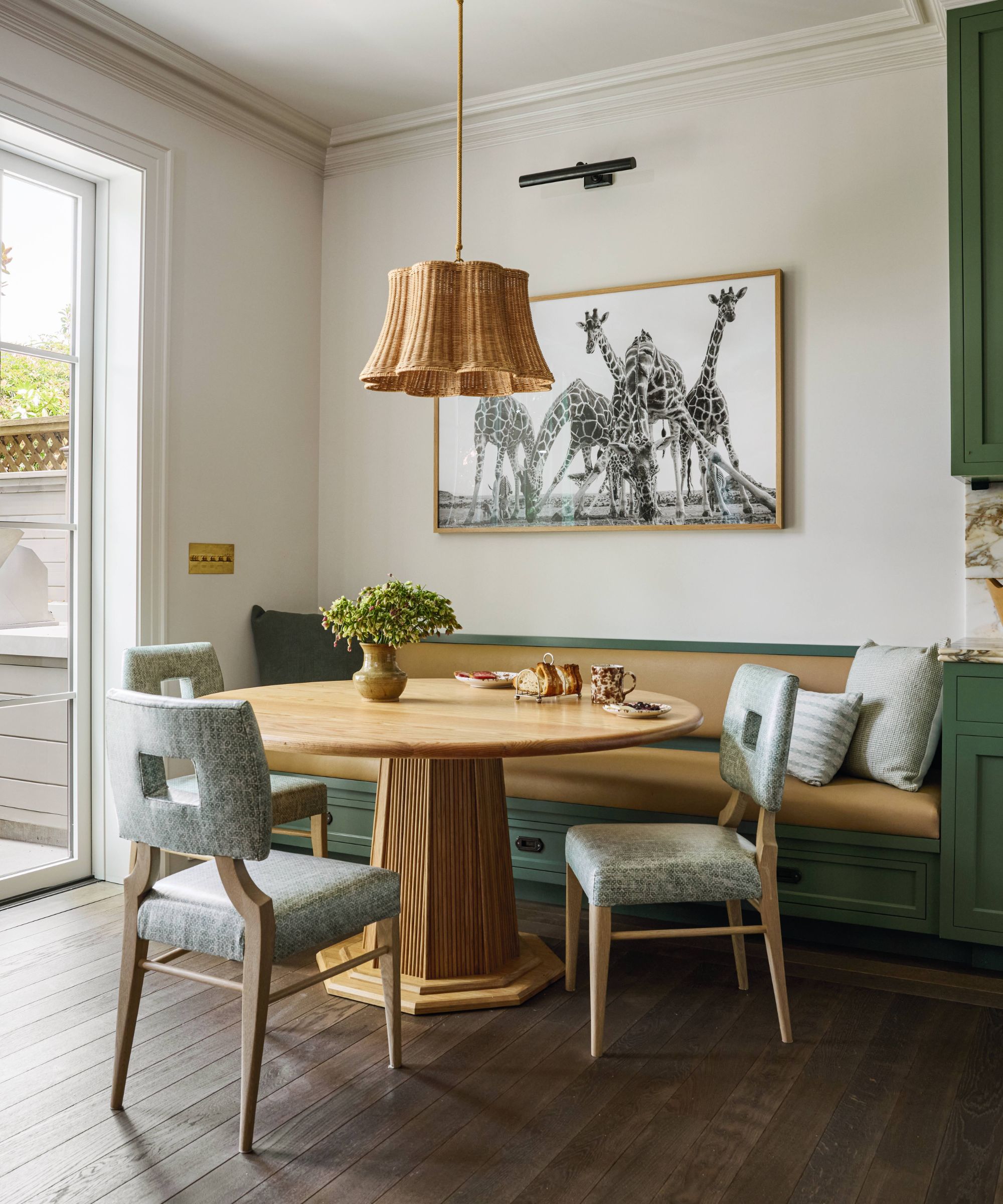 a neutral dining area in a kitchen with green cabinets and built in banquette dining nook with rounded table and rattan pendant