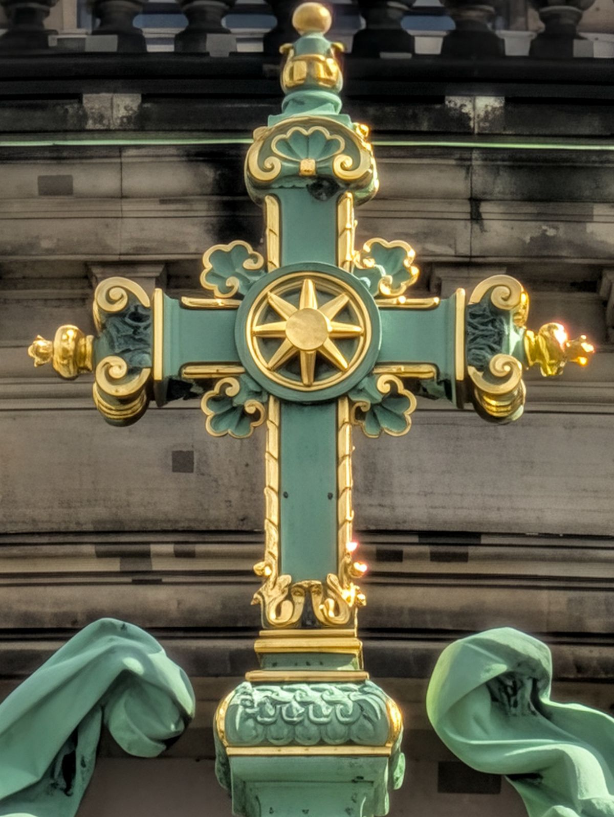 Close-up of an ornate green and gold cross with decorative scrollwork.