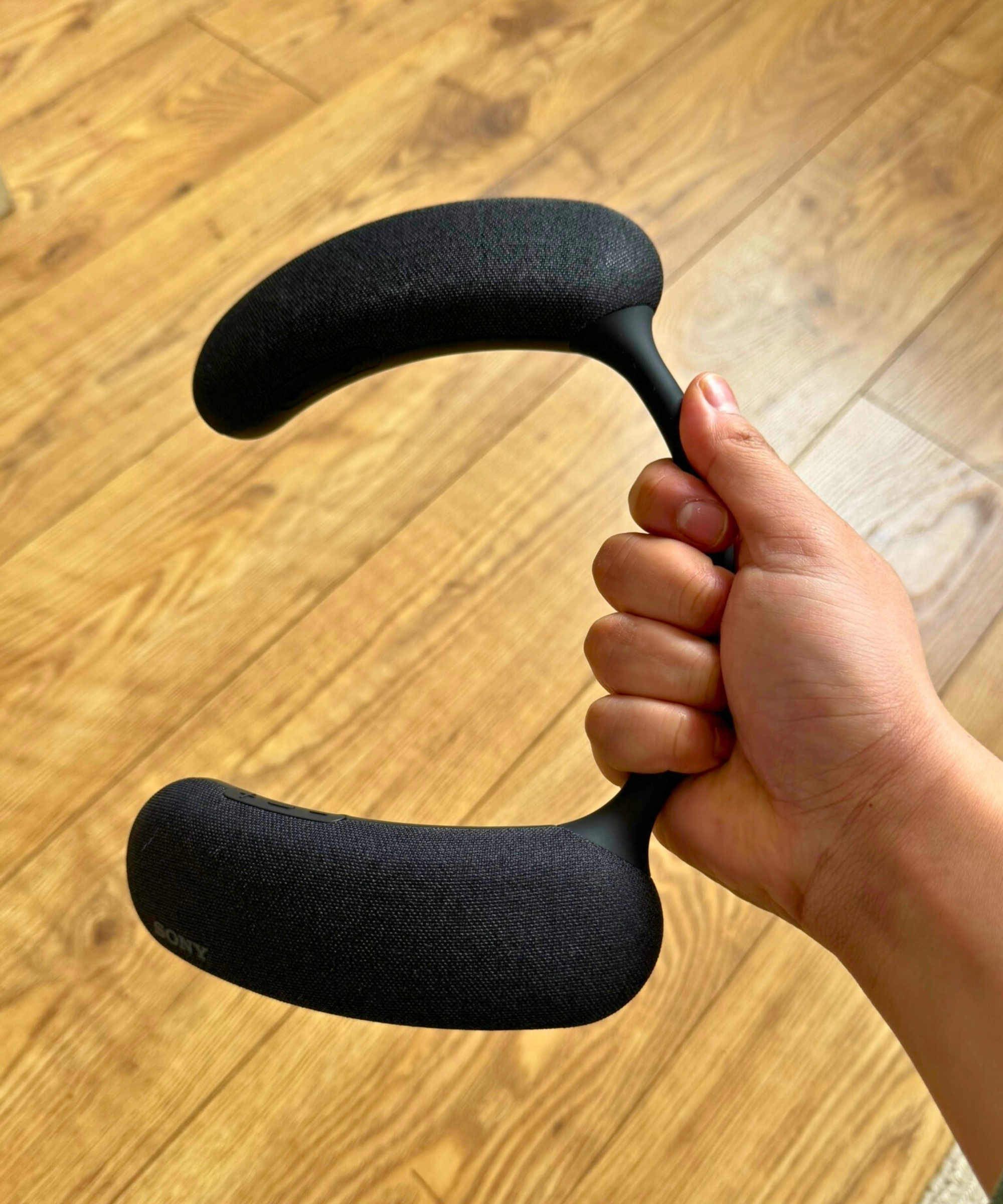 Hand holding the Sony BRAVIA Theater U above wooden floor.