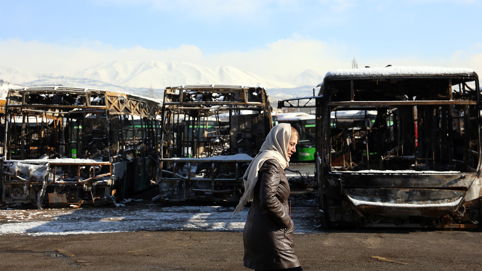 A woman walks past a depot of buses that were burned during recent anti-government protests in Tehran, Iran