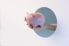 Hand holding a pink piggy bank, reaching out through a cut-out circle opening with blue background.